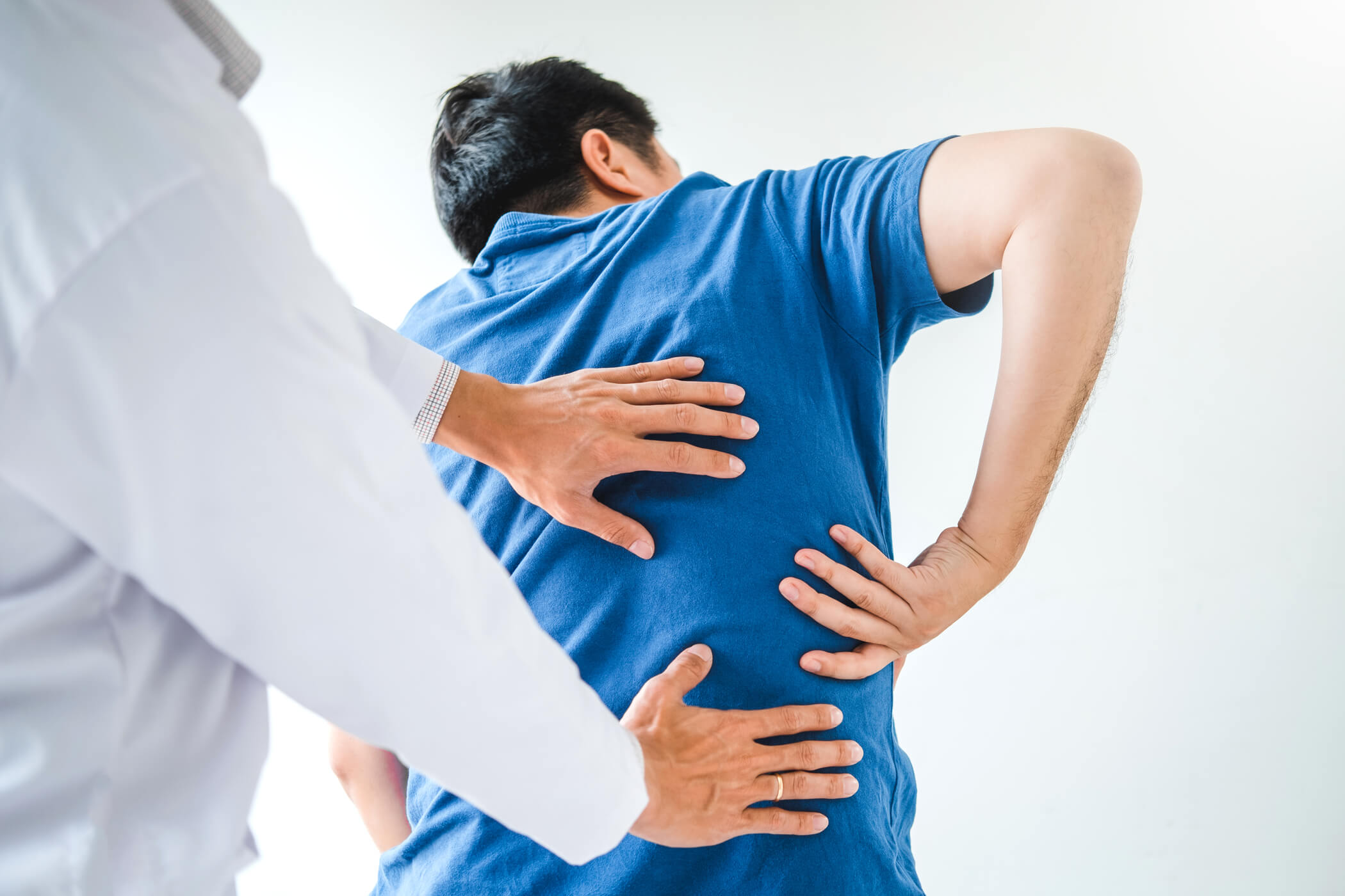 Man in blue t-shirt gripping back in pain.